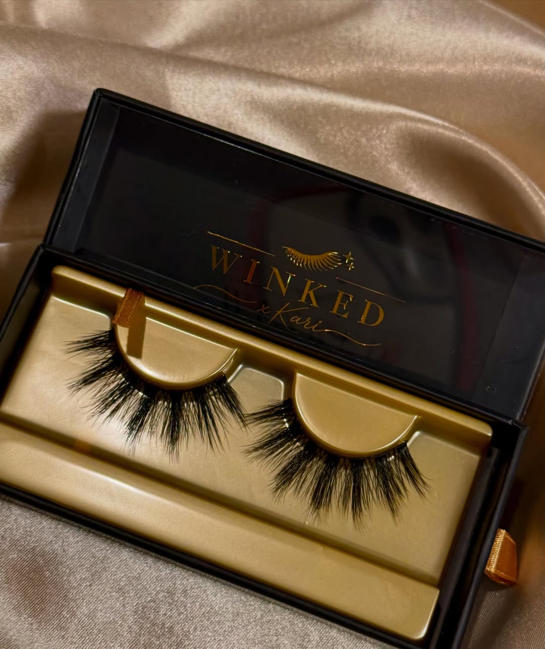 Fluffy Envy strip lashes inside an open black and gold Winked x Kari box on champagne satin